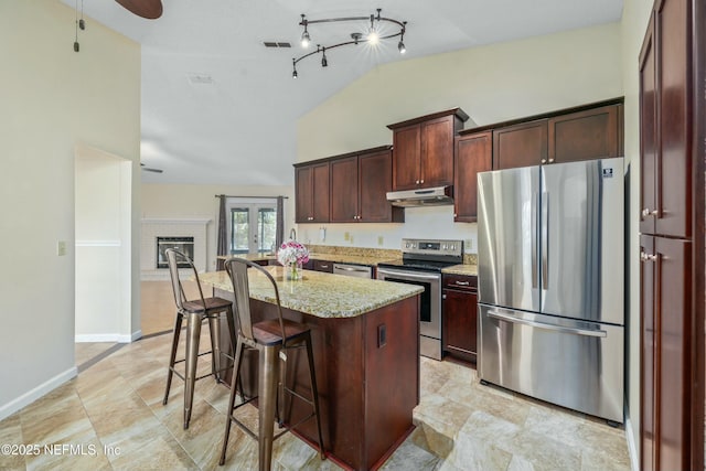 kitchen featuring light stone counters, under cabinet range hood, visible vents, appliances with stainless steel finishes, and a center island with sink