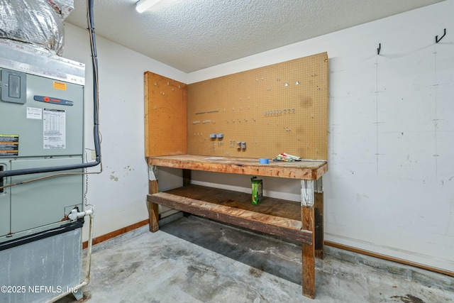 basement featuring heating unit, a textured ceiling, baseboards, and a workshop area