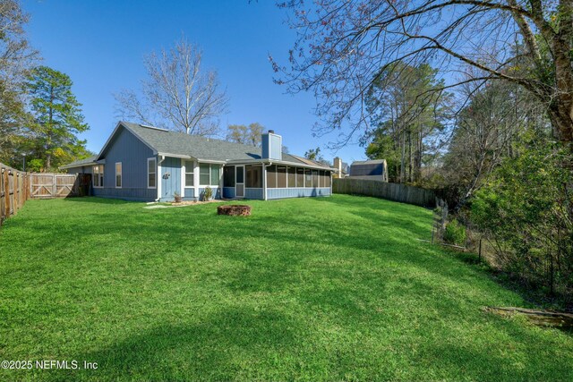 rear view of house with a yard, a chimney, a fenced backyard, and a sunroom