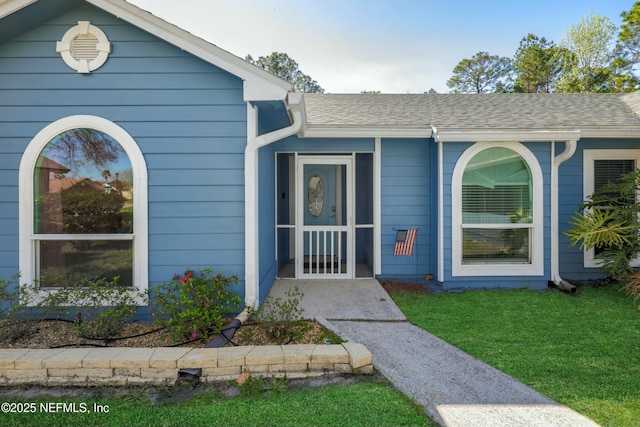 doorway to property featuring a shingled roof and a lawn