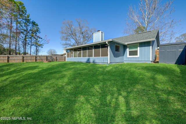 rear view of property featuring a storage shed, fence, a sunroom, a yard, and a chimney