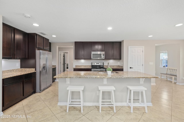 kitchen featuring light stone countertops, appliances with stainless steel finishes, a sink, recessed lighting, and light tile patterned floors