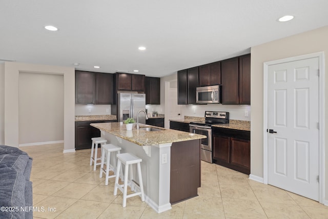 kitchen featuring a kitchen bar, appliances with stainless steel finishes, dark brown cabinets, a sink, and light tile patterned floors