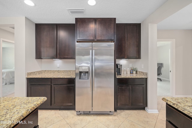 kitchen with dark brown cabinets, visible vents, stainless steel fridge, and light stone counters
