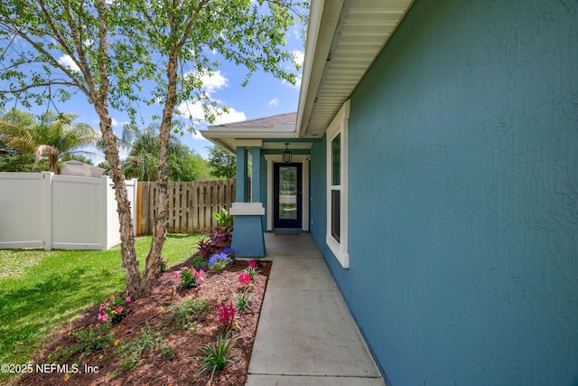view of exterior entry featuring stucco siding, fence, and a yard