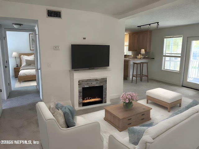 living room with light carpet, a stone fireplace, rail lighting, and visible vents