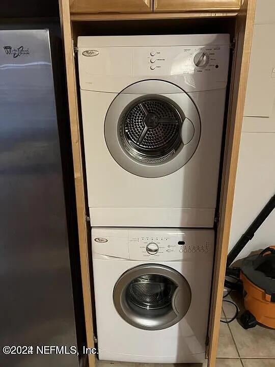 laundry area with stacked washer and dryer, tile patterned flooring, and laundry area