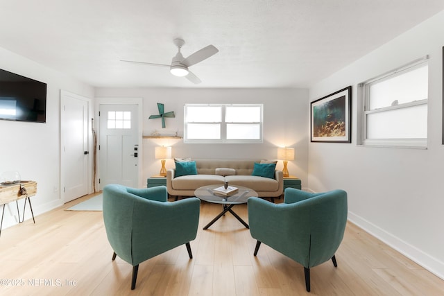 living area with a ceiling fan, light wood-style flooring, and baseboards