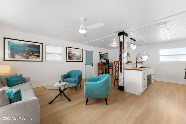 sitting room with light wood-style flooring, visible vents, baseboards, and a ceiling fan