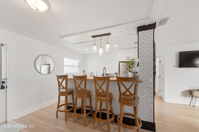 bar featuring visible vents, light wood finished floors, freestanding refrigerator, and wet bar