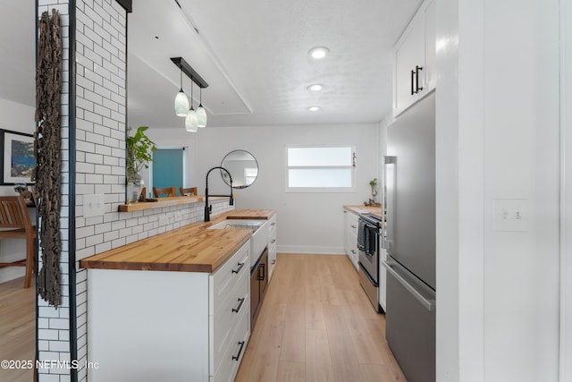 kitchen with stainless steel appliances, white cabinetry, wooden counters, and a sink