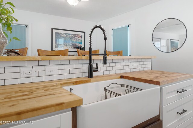 kitchen featuring tasteful backsplash, butcher block counters, and white cabinetry