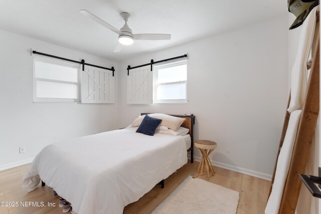 bedroom with light wood-style flooring, baseboards, a ceiling fan, and a barn door