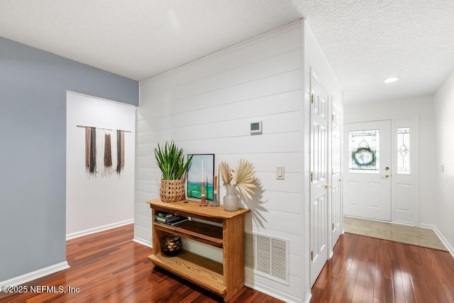 hall with hardwood / wood-style flooring, visible vents, baseboards, and a textured ceiling