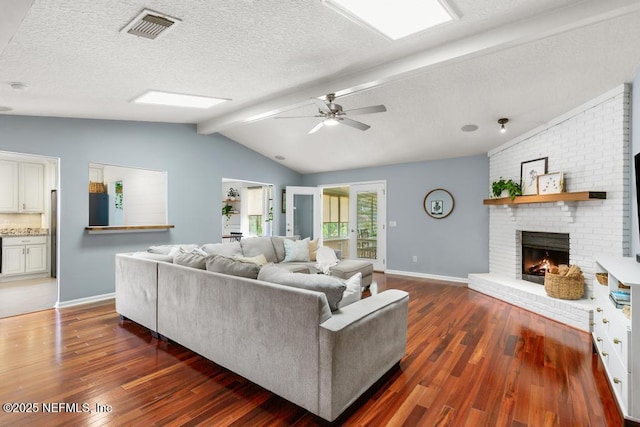 living area featuring visible vents, a textured ceiling, hardwood / wood-style floors, a fireplace, and vaulted ceiling with beams