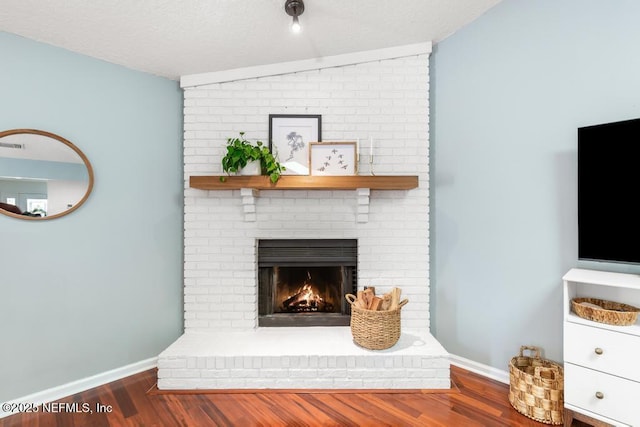 interior space featuring a fireplace, a textured ceiling, baseboards, and wood finished floors