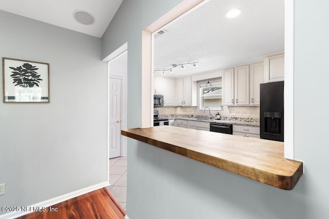 kitchen with a peninsula, a sink, decorative backsplash, black appliances, and wood counters