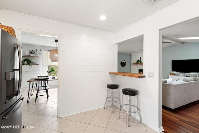 kitchen featuring light tile patterned flooring, stainless steel fridge, a textured ceiling, and a breakfast bar