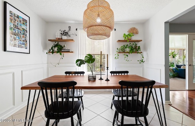 dining area featuring a wealth of natural light, a decorative wall, a textured ceiling, and light tile patterned flooring