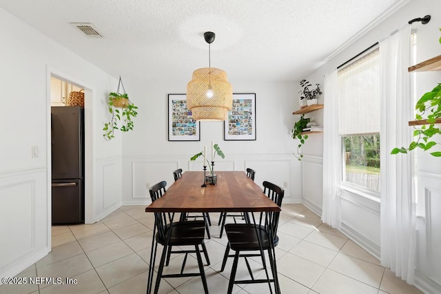 dining space featuring a textured ceiling, light tile patterned floors, visible vents, wainscoting, and a decorative wall