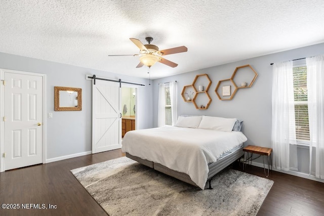 bedroom featuring a barn door, wood finished floors, baseboards, and a textured ceiling