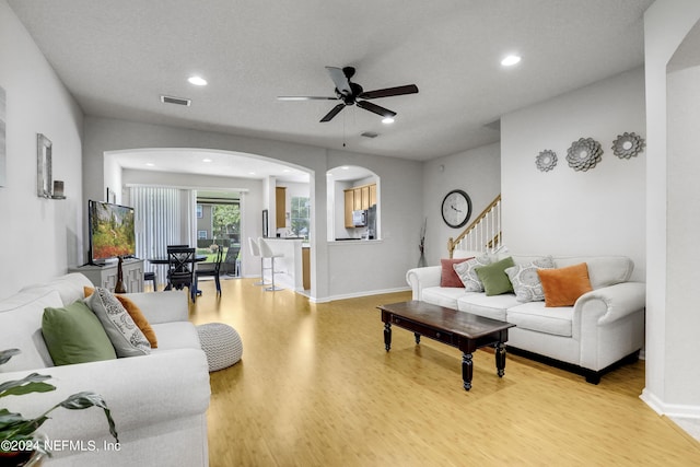 living area featuring visible vents, arched walkways, a ceiling fan, light wood-style flooring, and recessed lighting