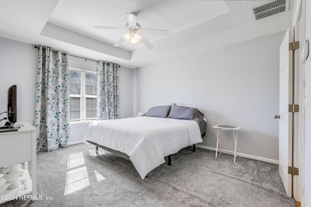 carpeted bedroom with a textured ceiling, ceiling fan, visible vents, baseboards, and a tray ceiling