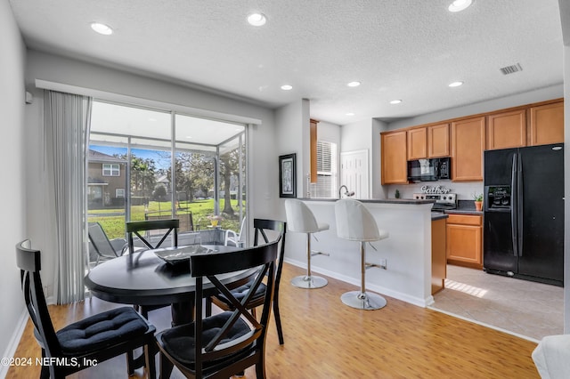 dining space featuring a textured ceiling, recessed lighting, a sunroom, baseboards, and light wood-style floors