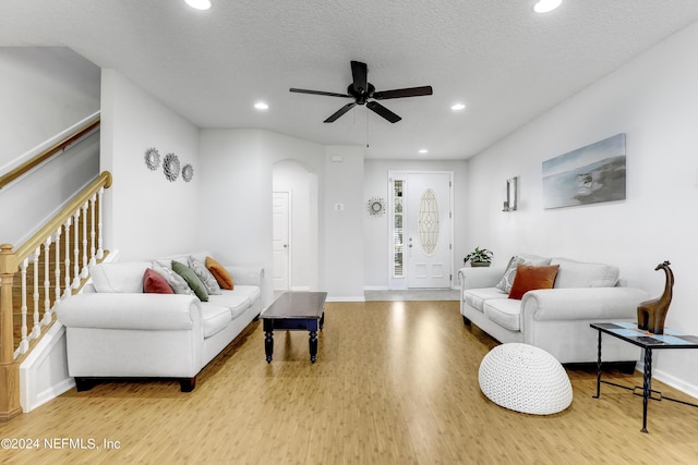 living room featuring arched walkways, a textured ceiling, recessed lighting, wood finished floors, and baseboards