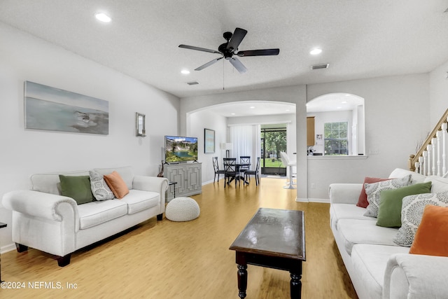 living room featuring light wood finished floors, stairs, visible vents, and arched walkways