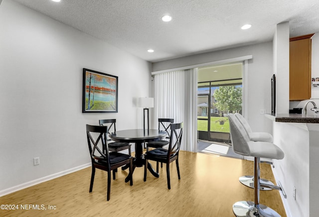 dining room with light wood finished floors, baseboards, a textured ceiling, and recessed lighting