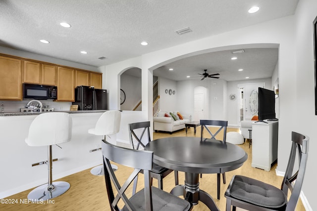 dining room featuring arched walkways, a textured ceiling, recessed lighting, and light wood-style floors