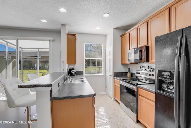 kitchen with dark countertops, a sink, black appliances, a peninsula, and a kitchen breakfast bar