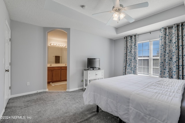 carpeted bedroom featuring a textured ceiling, connected bathroom, a ceiling fan, baseboards, and a raised ceiling