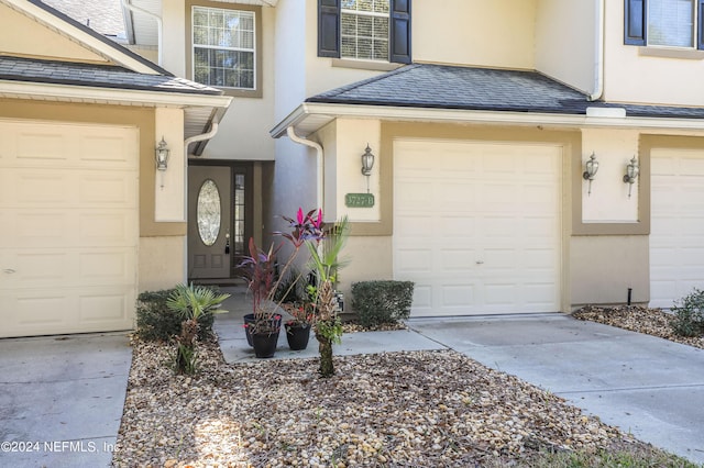 doorway to property featuring concrete driveway, roof with shingles, and stucco siding