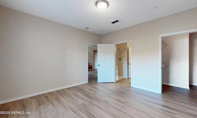 unfurnished bedroom featuring a closet, visible vents, light wood-style flooring, a spacious closet, and baseboards