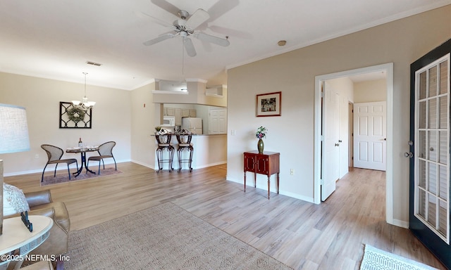 living area featuring light wood finished floors, baseboards, ornamental molding, and ceiling fan with notable chandelier