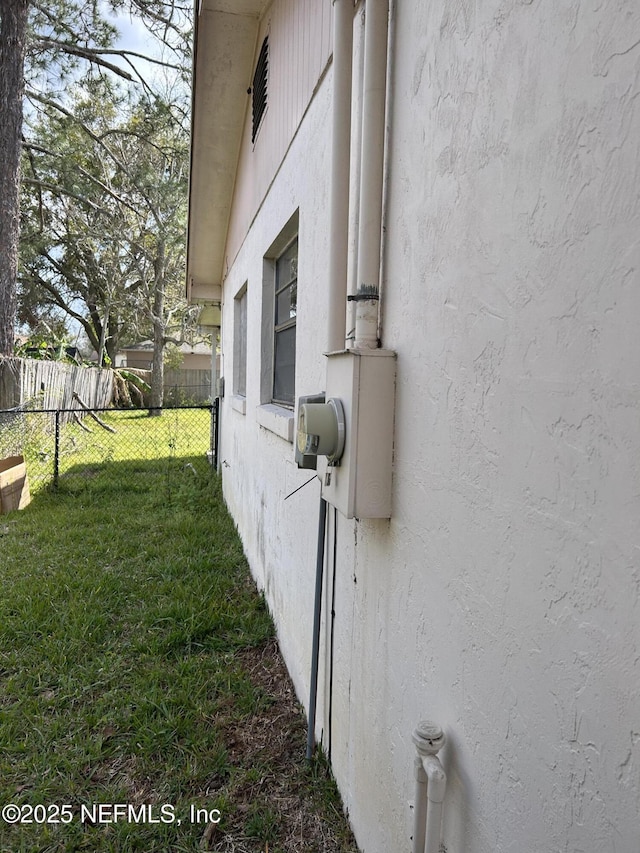 view of property exterior with stucco siding, a lawn, and fence