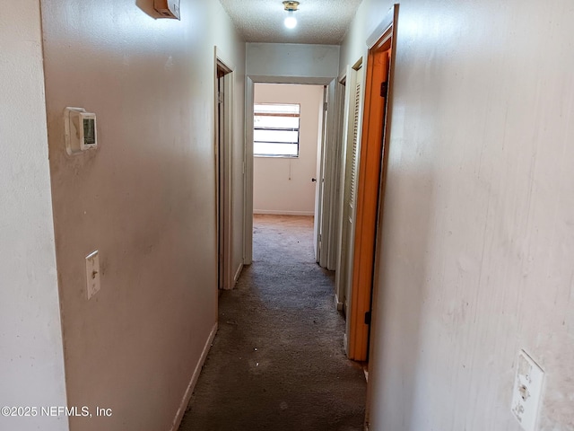 corridor featuring carpet, baseboards, and a textured ceiling