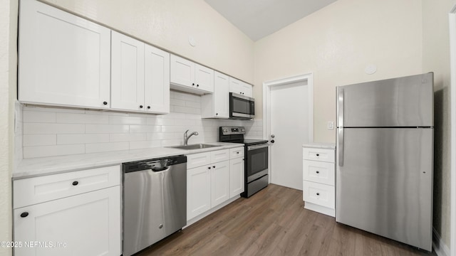 kitchen featuring wood finished floors, a sink, white cabinets, appliances with stainless steel finishes, and backsplash