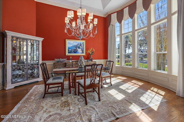 dining room featuring wood finished floors, an inviting chandelier, a towering ceiling, and a decorative wall