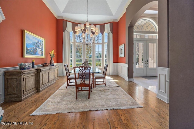 dining room featuring a wainscoted wall, hardwood / wood-style floors, french doors, arched walkways, and an inviting chandelier