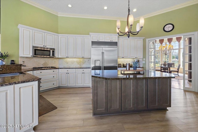 kitchen with a notable chandelier, ornamental molding, a sink, appliances with stainless steel finishes, and decorative backsplash