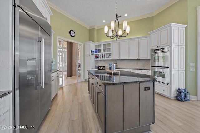 kitchen with tasteful backsplash, ornamental molding, dark stone countertops, appliances with stainless steel finishes, and an inviting chandelier