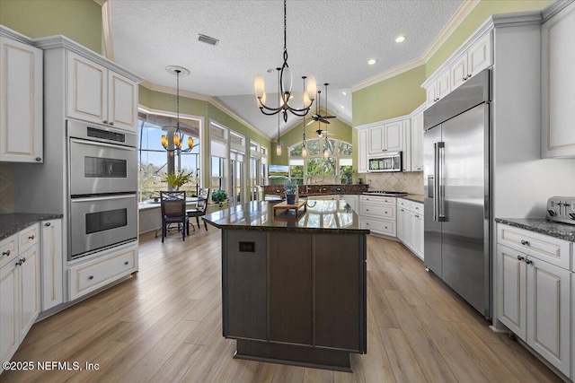 kitchen with light wood finished floors, an inviting chandelier, stainless steel appliances, vaulted ceiling, and backsplash