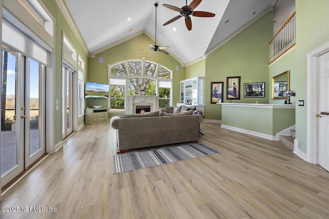 living area featuring a ceiling fan, wood finished floors, a warm lit fireplace, and high vaulted ceiling