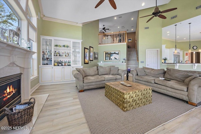 living area with crown molding, a high ceiling, light wood finished floors, and ceiling fan