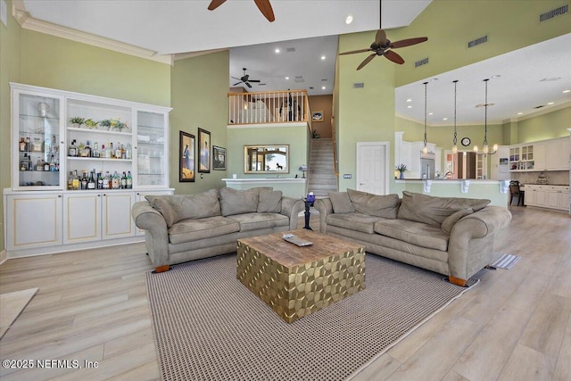 living area featuring visible vents, crown molding, light wood-style flooring, a towering ceiling, and a ceiling fan