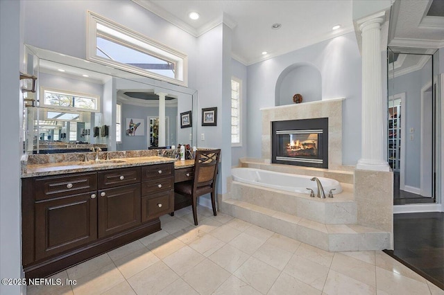 full bathroom with a garden tub, ornamental molding, decorative columns, a tile fireplace, and vanity