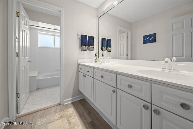 bathroom with a sink, wood finished floors, double vanity, baseboards, and shower / bathtub combination